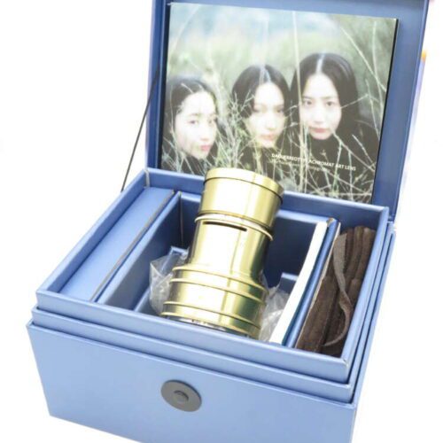 Blue box containing a brass camera lens, with a photograph of three women in the lid.