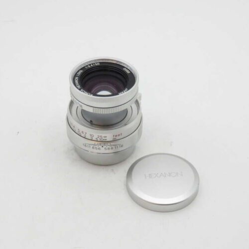 Silver camera lens and lens cap on white background. Lens markings read "Hexanon Lens 1:2.4/50."