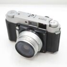 A silver and black Fujifilm camera with a large lens, featuring various dials and a viewfinder on a white background.