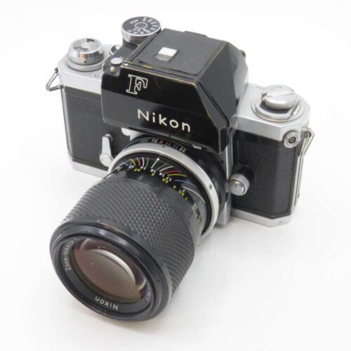 A vintage Nikon F black and silver camera with a large lens attached, featuring manual dials and a textured grip, photographed on a white background.