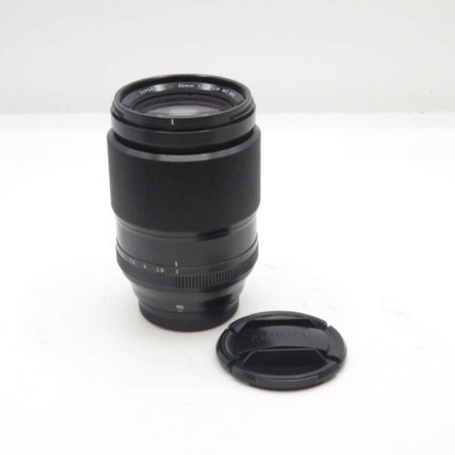 Black camera lens with a lens cap on a white surface.