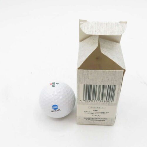 White golf ball with a blue logo and text "MINOLTA" next to an open cardboard box with a barcode and Japanese text.