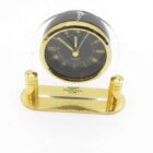 Gold and black quartz desk clock with clear plastic arch and base labelled "Hanimex 1912 - 1987".