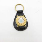 Gold pocket watch with Roman numeral display, set in black leather case with a key ring attached.