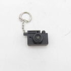 Miniature black camera keychain with a lens and small chain attached to a silver keyring.
