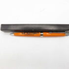 Orange pen with black writing that reads "UNOMAT INTERNATIONAL," placed beside a black case on a white background.