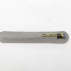 Gold tie clip with "Quality Optics" written on it, placed on a grey fabric case.