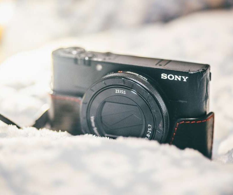 Sony digital camera with Zeiss lens in a black and red case, resting on a textured white surface.