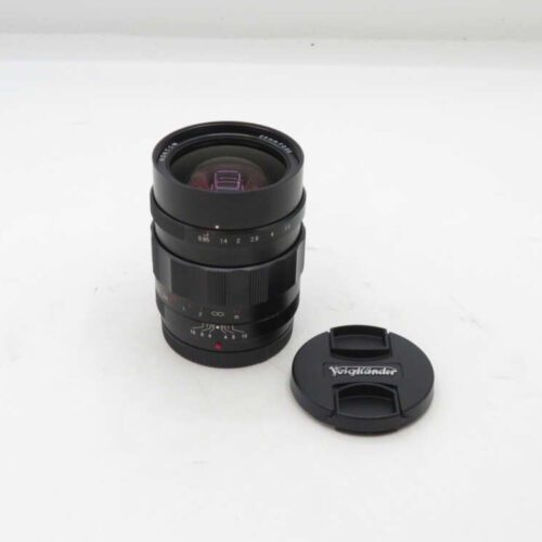 A Voigtlander camera lens with its cap placed beside it on a white background.