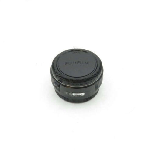 Black Fujifilm camera lens with a cap placed on a white surface.