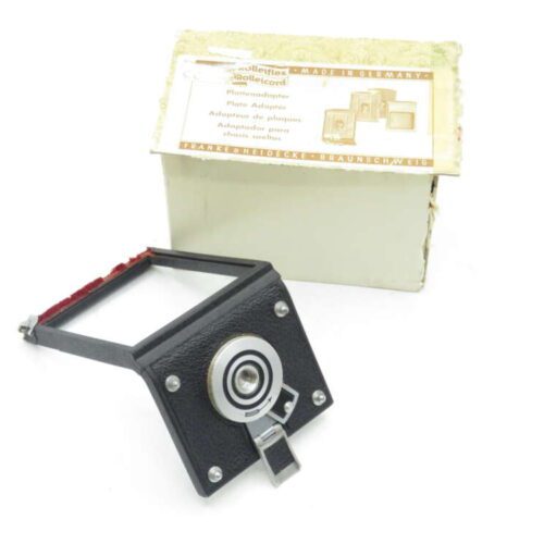 Camera plate adapter in front of a vintage white box with German and English text