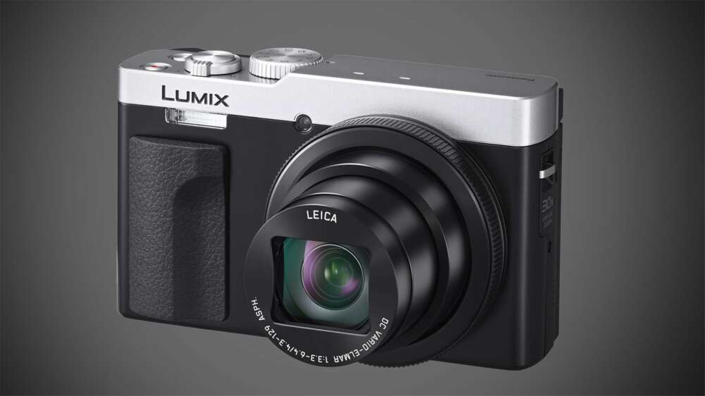 A Lumix camera with a Leica lens, featuring a compact design with a silver top and black body, and prominently displayed control dials and textured grip on the left side.