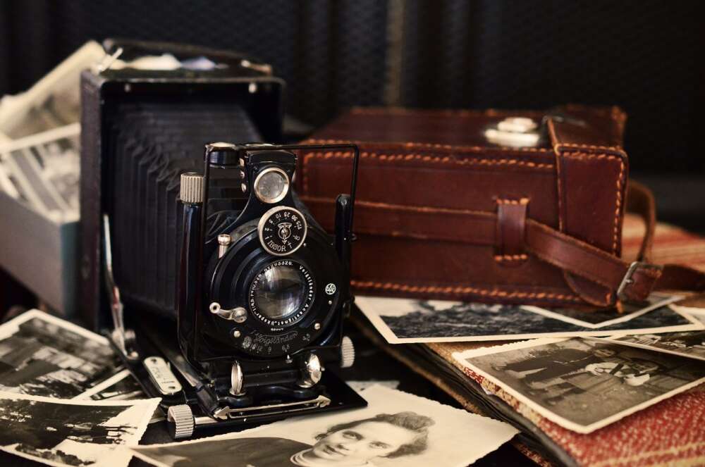Vintage camera with bellows, surrounded by old photographs and a leather case.