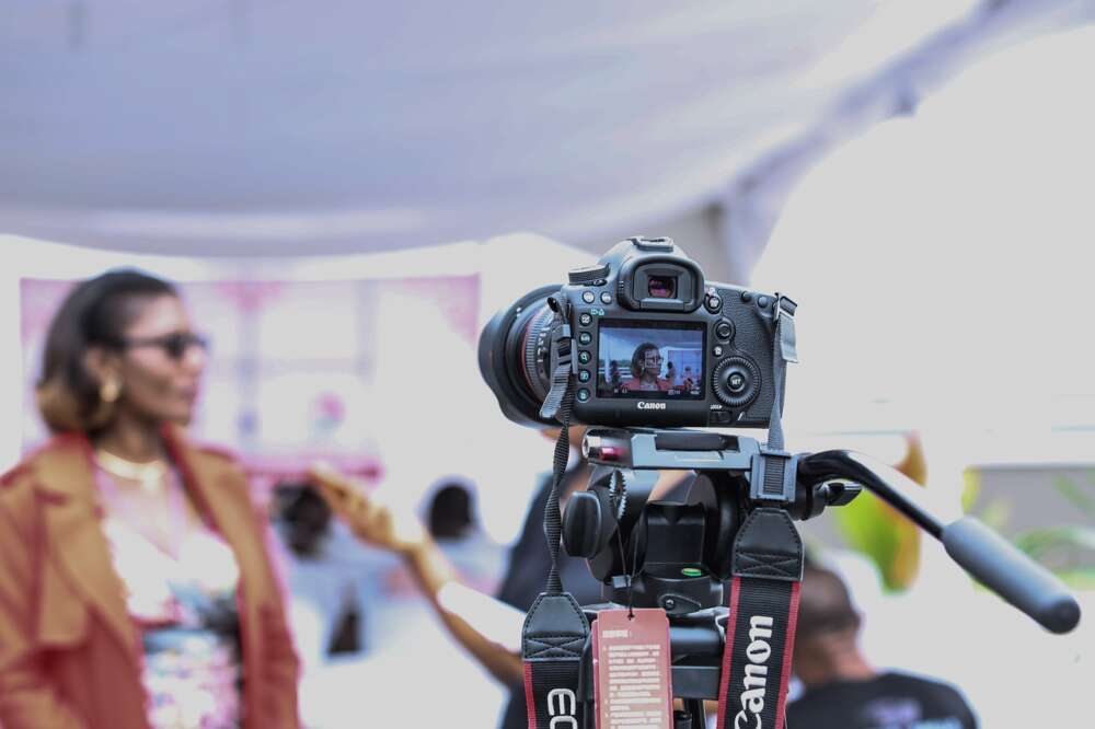 A digital camera on a tripod filming a person in the background.