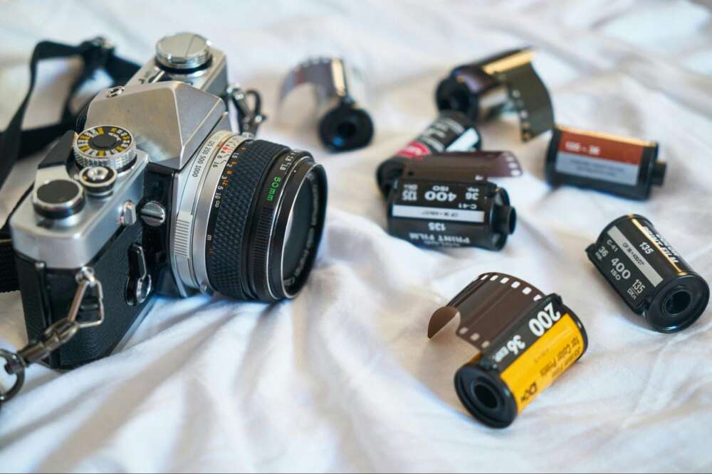 Vintage film camera with several rolls of 35mm film on a white surface.