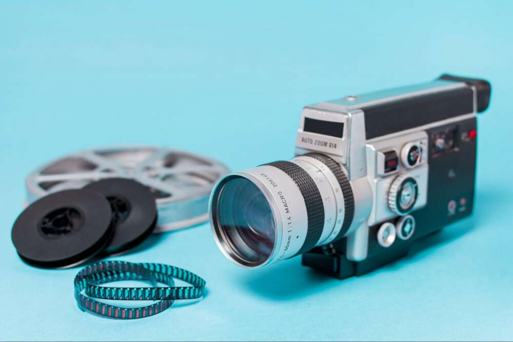 Vintage video camera with film reels and a filmstrip against a blue background.