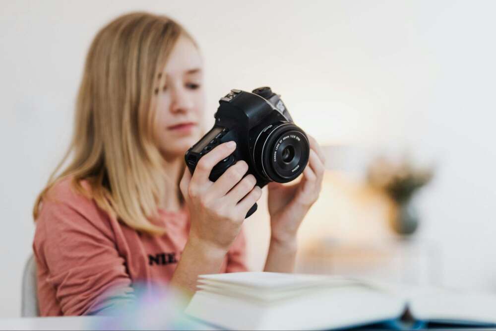 A person holding a DSLR camera, focusing on it indoors.