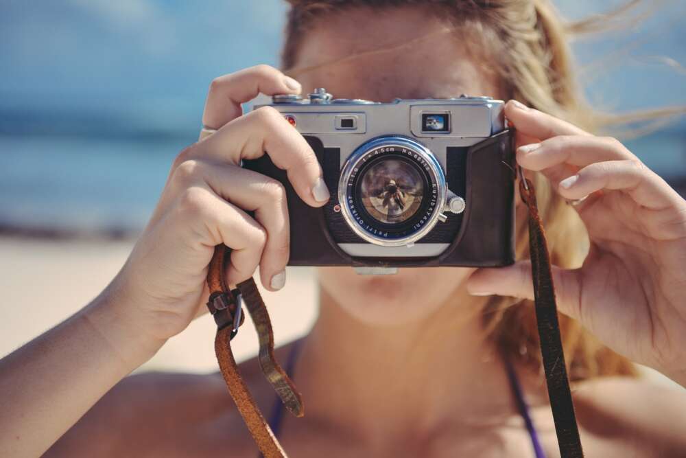 Person holding a vintage camera, beach in the background.