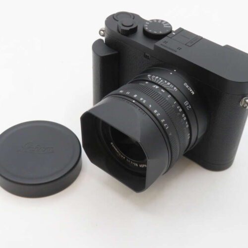 Black Leica camera with a lens cap beside it.