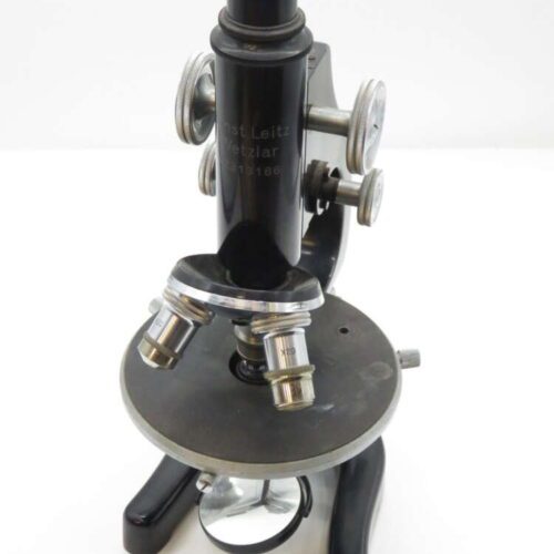Vintage black microscope with dual lenses, silver adjustment knobs, and a round base with a reflective mirror underneath.