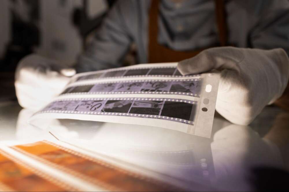 Person wearing white gloves examining film negatives on a light table.