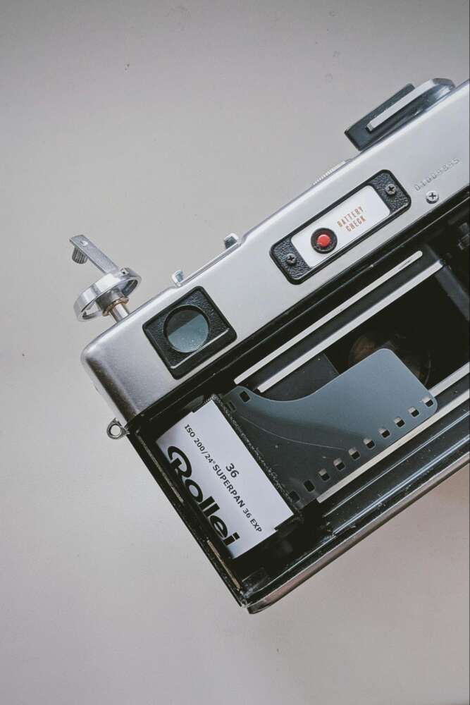 A close-up of an open vintage camera with a roll of Rollei superpan 200 film inside.