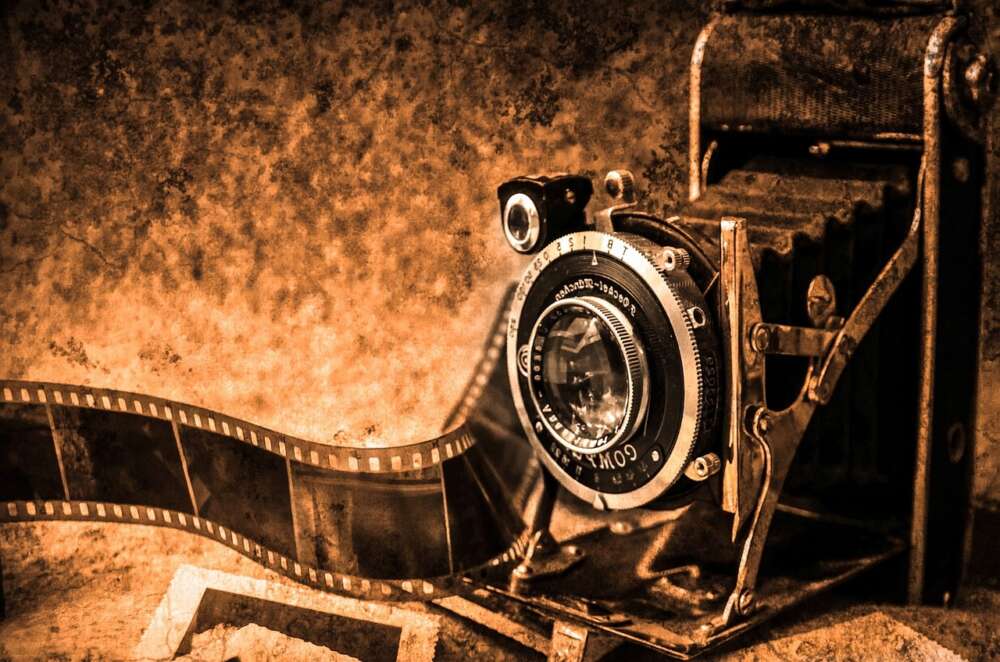 Vintage camera with an extended bellows and old film strip on a textured sepia-toned background.