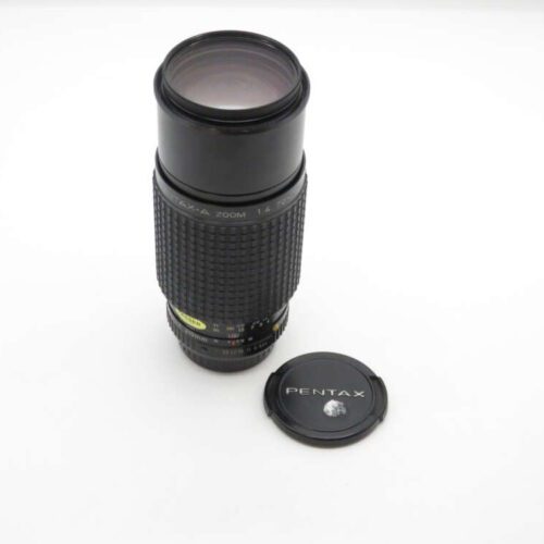 Pentax lens with detached lens cap on a white surface.