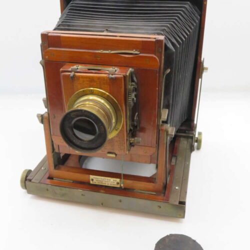 Vintage wooden large format camera with bellows and brass lens, placed on a white background.