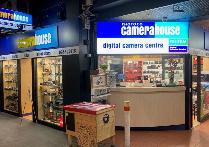 CameraHouse digital camera centre shopfront with illuminated signage, displaying cameras, binoculars, and accessories in the windows.