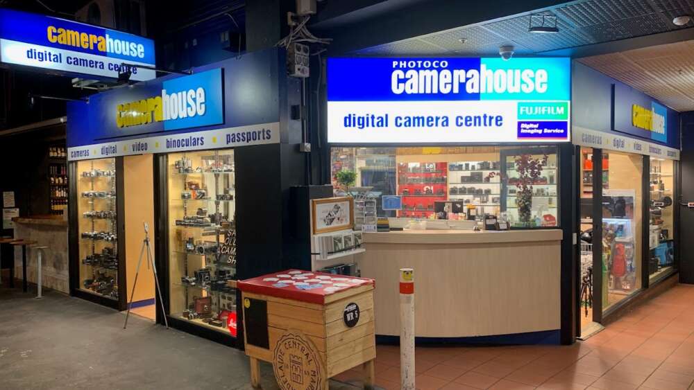 CameraHouse digital camera centre shopfront with illuminated signage, displaying cameras, binoculars, and accessories in the windows.