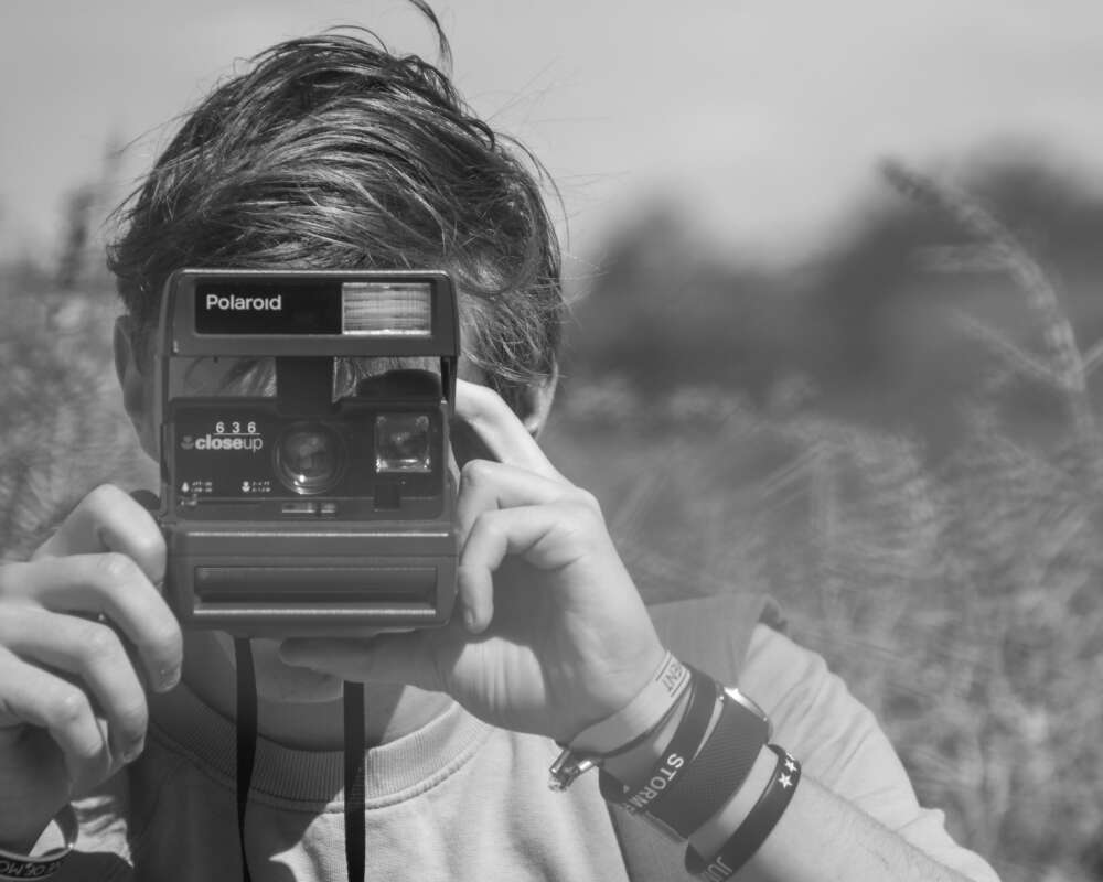 A person holding a Polaroid camera up to their face in an outdoor setting.