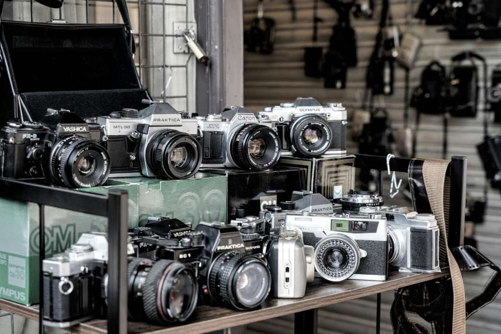 A collection of vintage cameras displayed on a shelf at a market stall.
