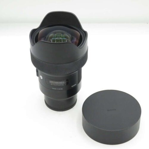 A Sigma 14mm f/1.8 DG HSM Art wide-angle lens with its protective cap beside it on a white surface.