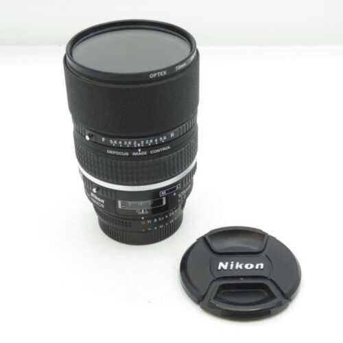 A Nikon camera lens with defocus image control, positioned upright, alongside a detached Nikon lens cap.