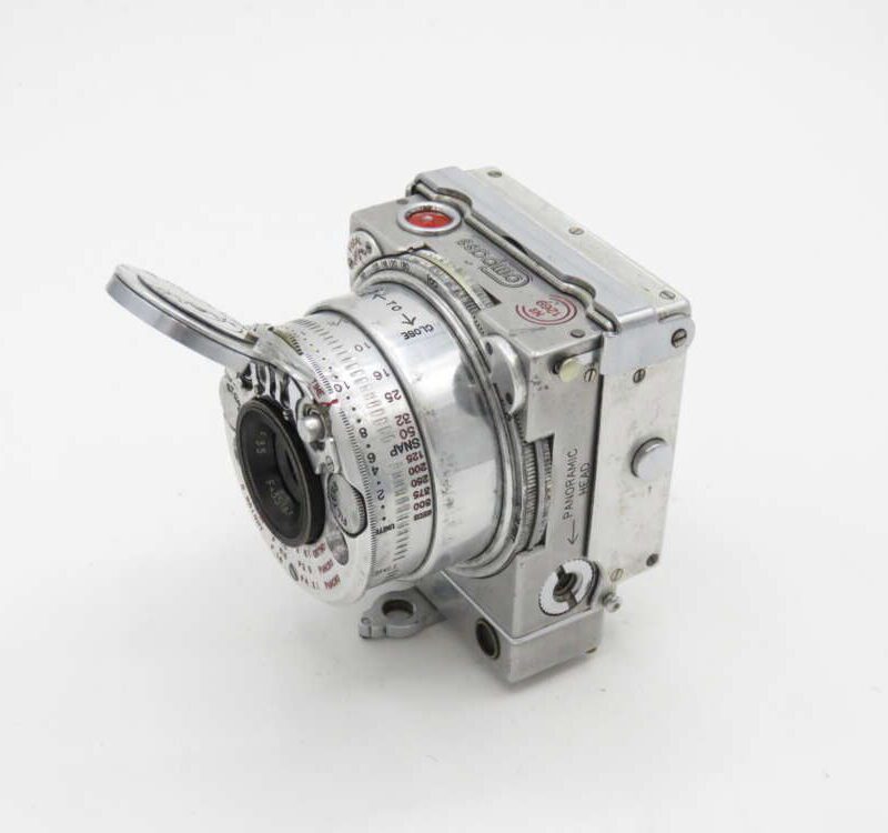 Vintage metal camera with a protruding lens and various dials and markings.