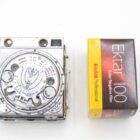 A vintage camera light meter next to a box of Kodak Ektar 100 color negative film.