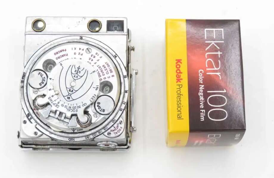 A vintage metal camera mounted exposure meter next to a box of Kodak Ektar 100 color negative film.