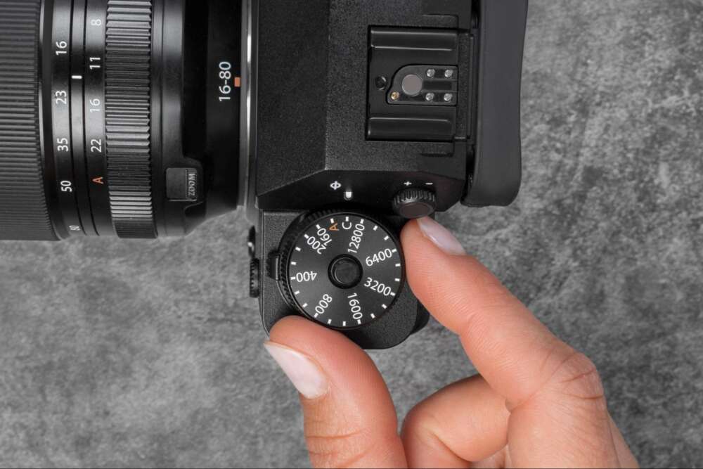 A hand adjusting the ISO dial on a DSLR camera with a 16-80mm lens.