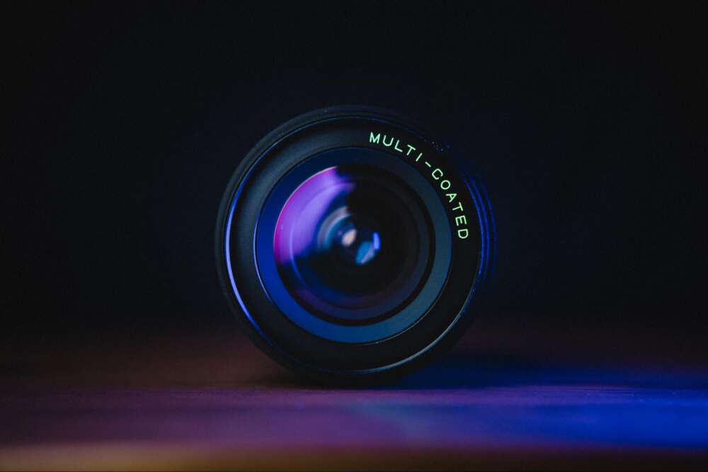 A close-up view of a camera lens with "MULTI-COATED" text, reflecting blue and purple hues against a dark background.