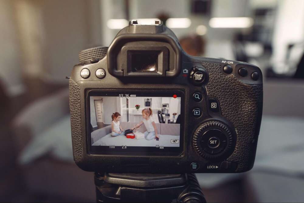 A camera displays a video of two children sitting on a couch, playing with a toy.