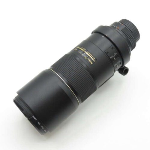 A black Nikon camera lens with a zoom feature placed on a white surface.