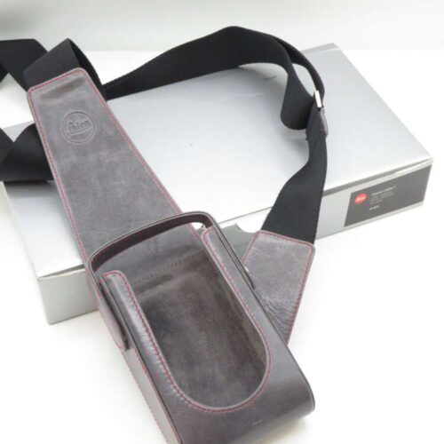 A leather camera bag with a black strap and red stitching, displayed on a silver box.