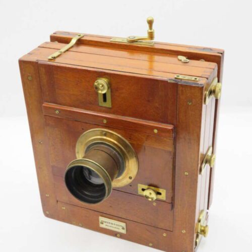 An antique wooden box camera with brass fittings and a prominent lens, featuring a polished wooden exterior and metal knobs for adjustments.