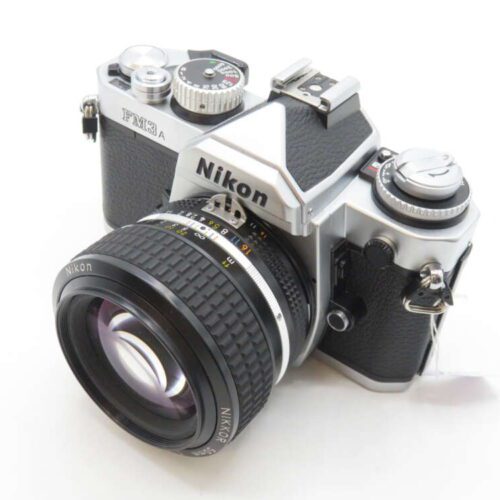 A silver and black Nikon FM3A film camera with a Nikkor lens attached, viewed from an angle showing its top controls and dials.