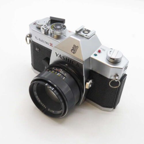 A vintage Yashica TL Electro X 35mm film camera with a black and silver body, featuring a Yashinon 50mm f/1.4 lens, placed on a white surface.