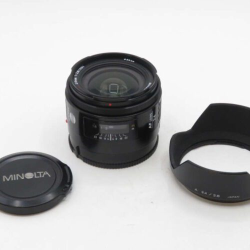 A Minolta AF lens with a lens cap and a lens hood placed beside it on a white surface.