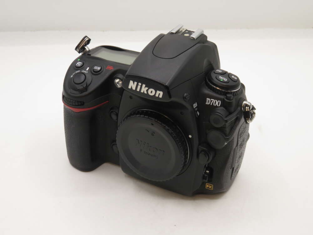 IMG_0408 A Nikon D700 DSLR camera with various buttons and dials visible, resting on a white surface.
