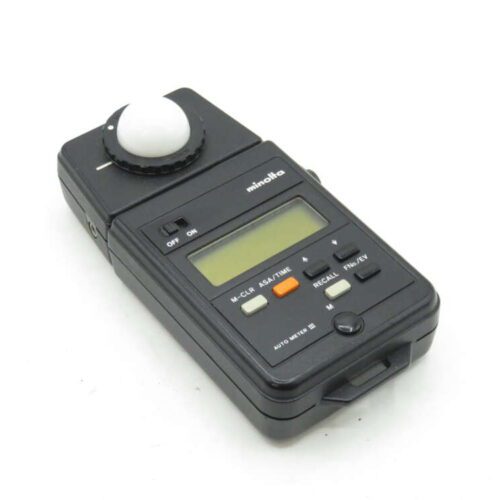 A Minolta Auto Meter III light meter, featuring a black rectangular body, a light sensor dome on top, and a digital display with several buttons including on/off and function settings.