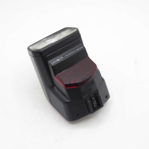 A Minolta Program 3200i external camera flash unit with a black rectangular body and a translucent white diffuser at the top. It features a red translucent section below the flash and a metal attachment bracket at the base.